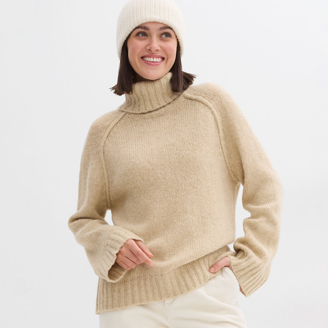 Gemütlicher beiger Rollkragenpullover mit weißer Mütze.