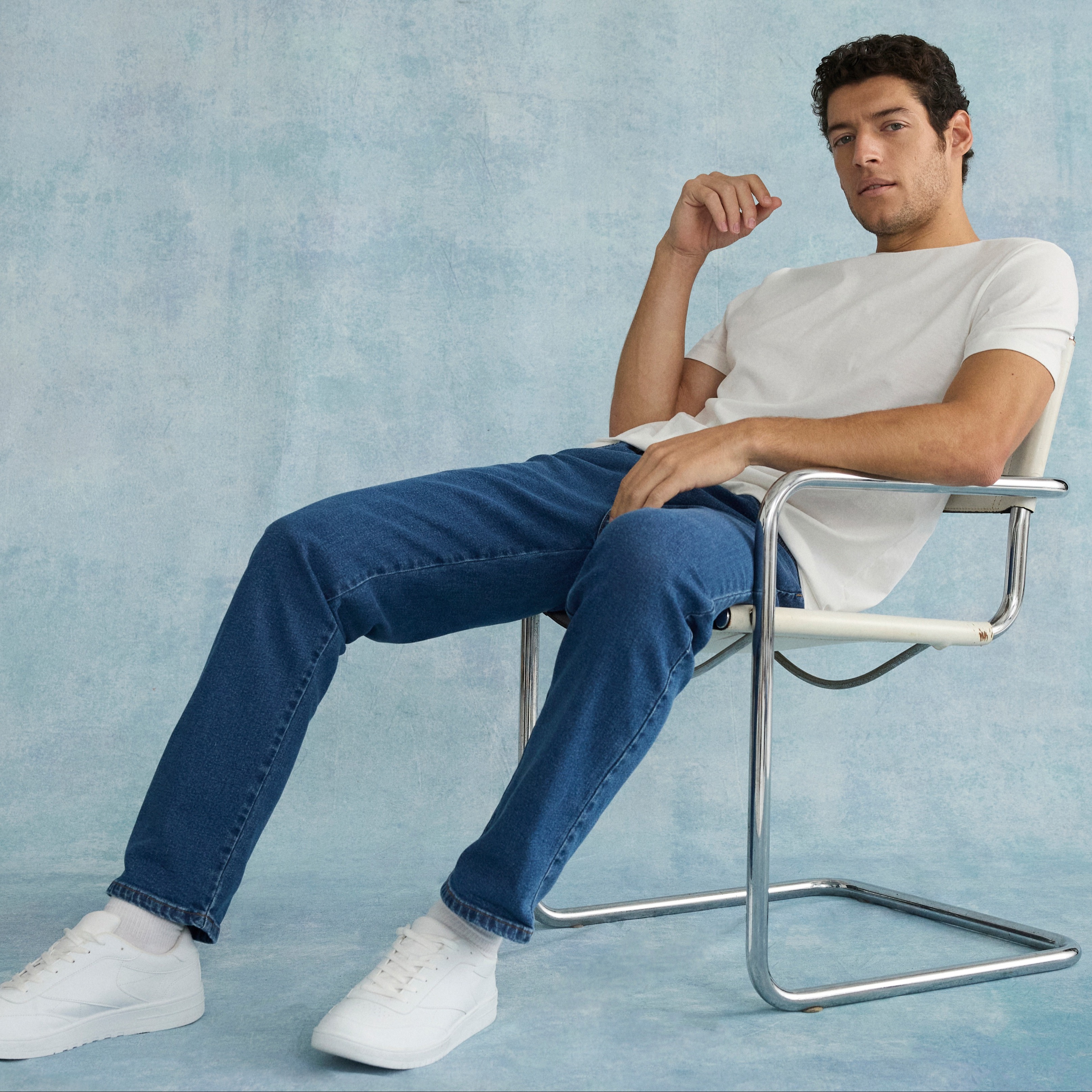Lässiger Look: Weißes T-Shirt, blaue Jeans und weiße Sneakers auf einem modernen Stuhl.