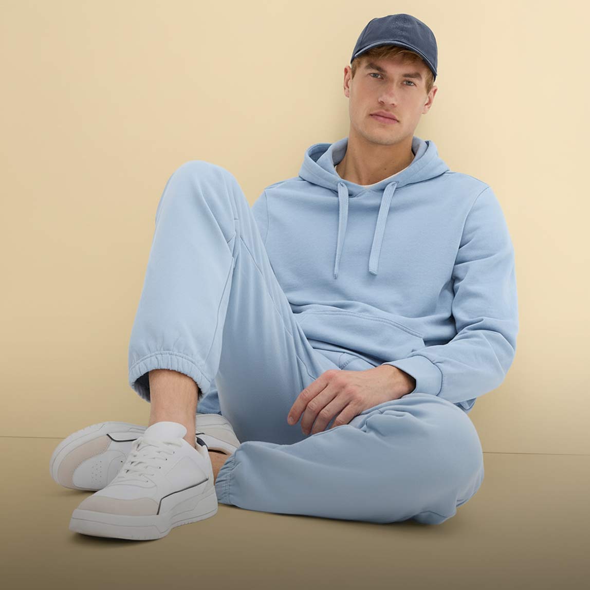 Hellblauer Kapuzenpullover und Jogginghose, ergänzt durch weiße Sneaker und blaue Kappe.
