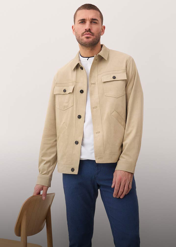 Beige VelourslederimitatJacke mit Brusttaschen, weißes T-Shirt und blaue Hose.