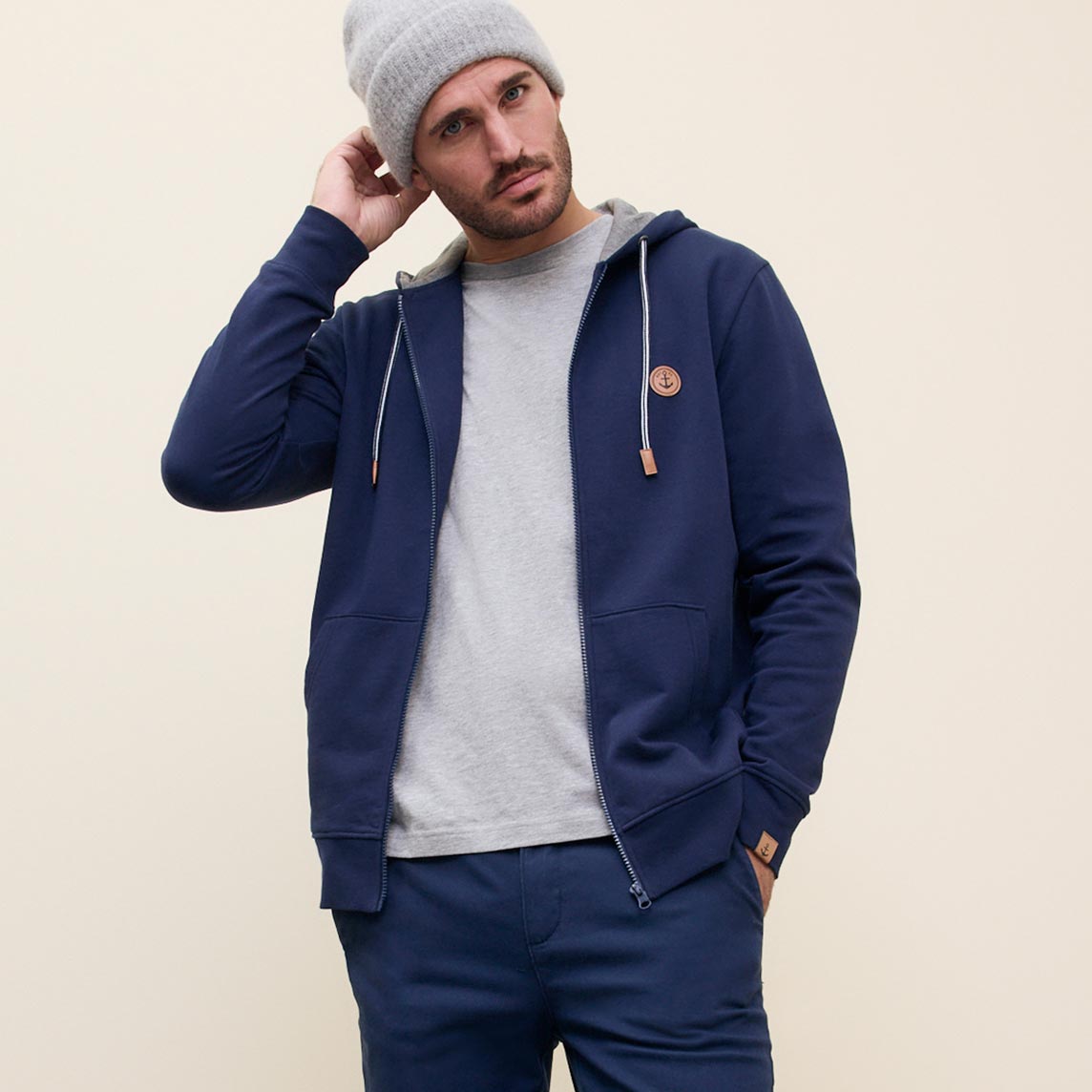 Lässiger Look mit blauer Kapuzenjacke, grauer Mütze und hellem Pullover.