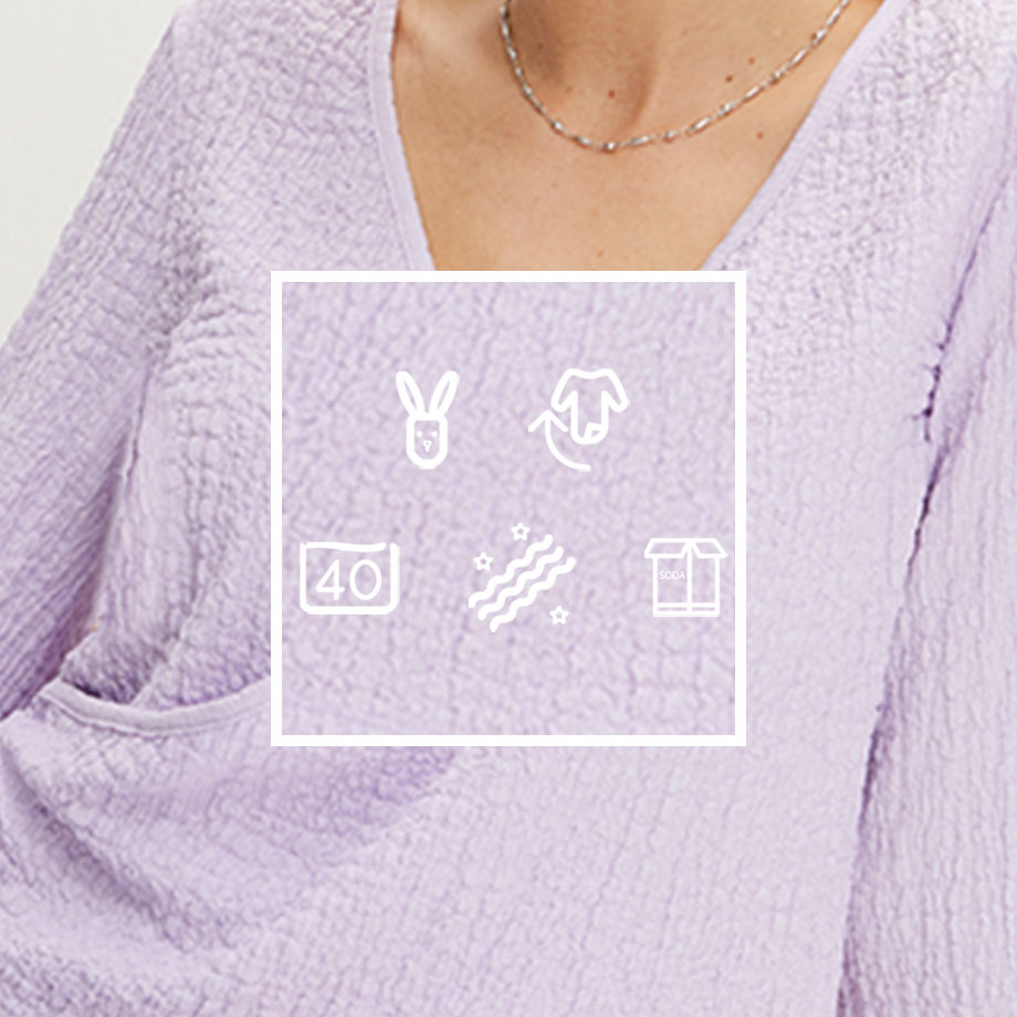 Zarter lila Pullover mit V-Ausschnitt, weichen Ärmeln und feiner Halskette als Accessoire.