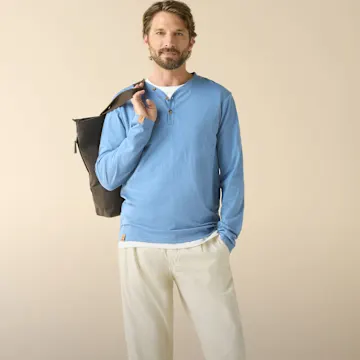 Hellblaues Langarmshirt, helle Hose und eine dunkle Umhängetasche.