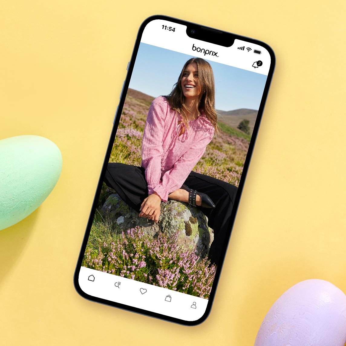 Rosafarbene Bluse mit Knöpfen, dunkle Hose und silberne Armreife in ländlicher Umgebung.