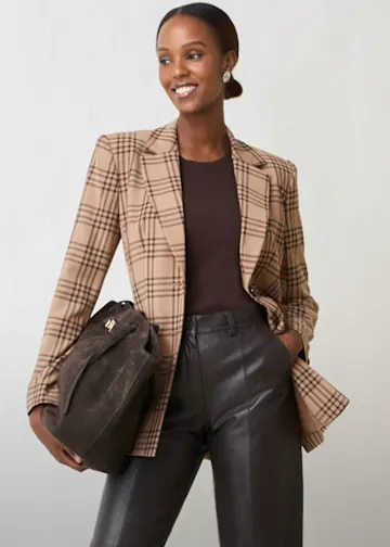 Karierter Blazer, dunkles Top, Lederhose und Wildleder-Tasche ergeben einen schicken Look.