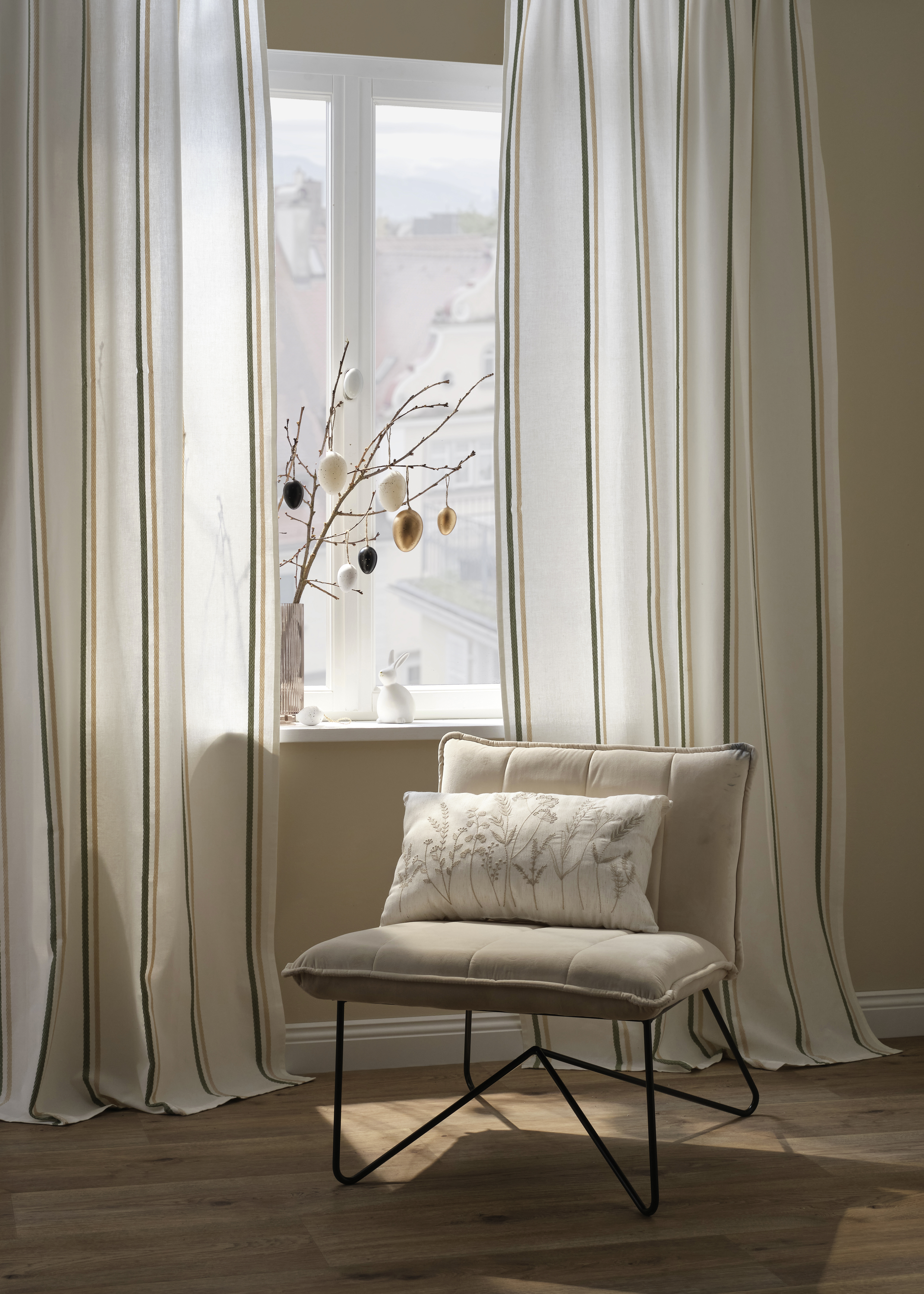Eleganter cremefarbener Sessel vor bodenlangen Vorhängen. 