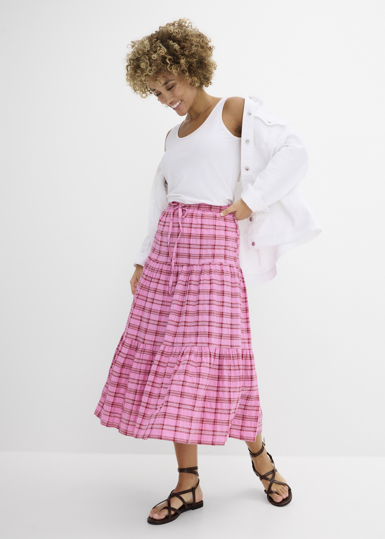 Weißes Tanktop, pinker Karorock, weiße Jacke und braune Riemchensandalen.