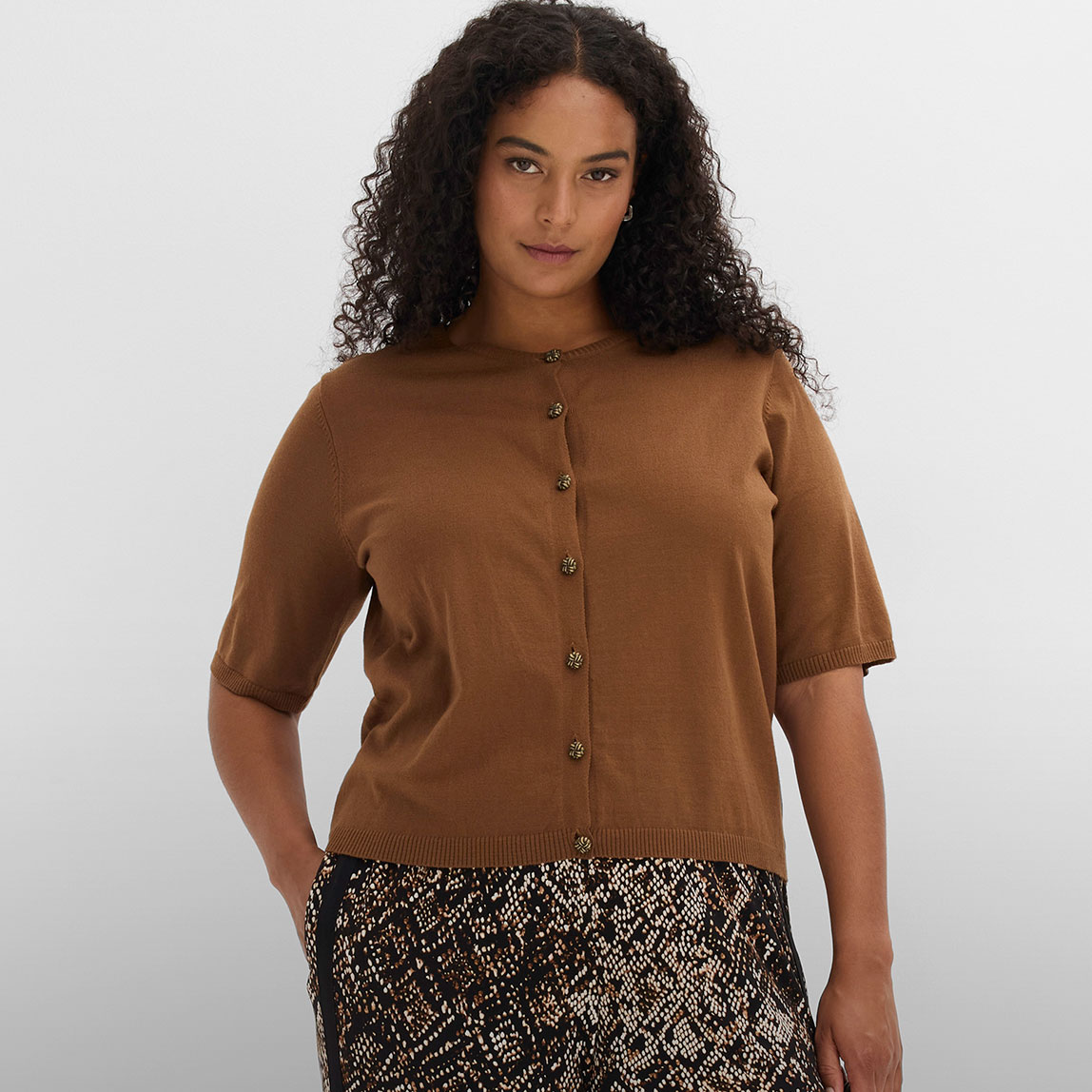 Braune Strickjacke mit kurzen Ärmeln und Knöpfen zur gemusterten Hose.