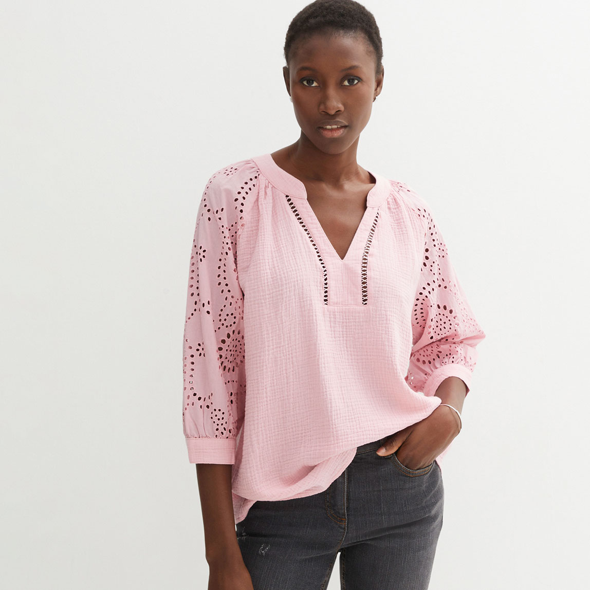 Rosa Tunika mit Lochstickerei und V-Ausschnitt, kombiniert mit dunkler Jeans.