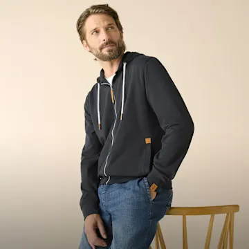 Mann trägt blaue Jeans und dunklen Kapuzenpullover mit Reißverschluss.