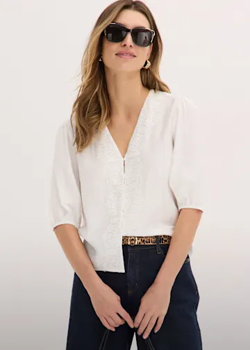 Weiße Bluse mit zarter Stickerei, dunkle Jeans und gemusterter Gürtel.