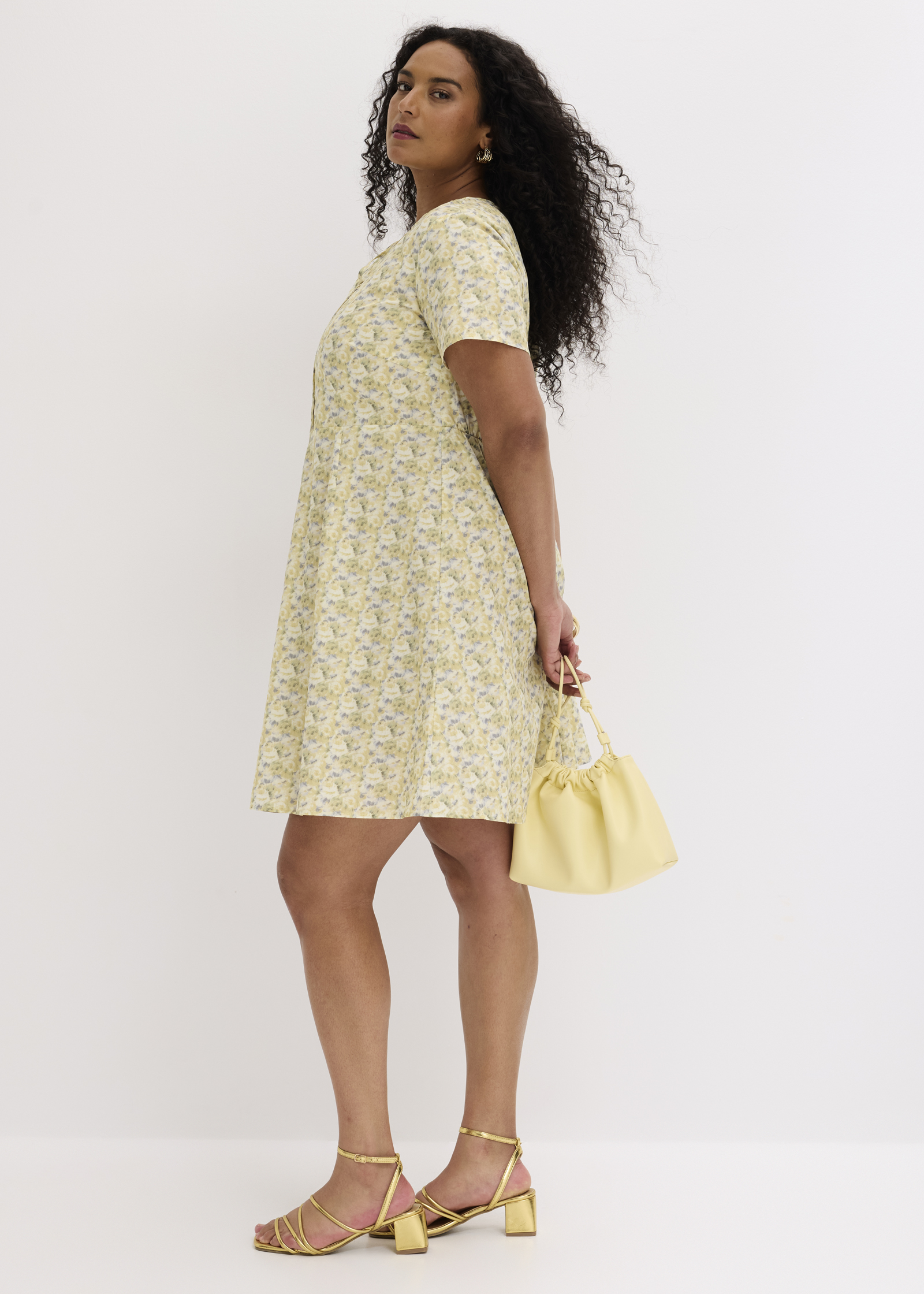 Ein leichtes gelbes Blumenkleid, goldene Riemchensandalen und eine gelbe Beuteltasche.