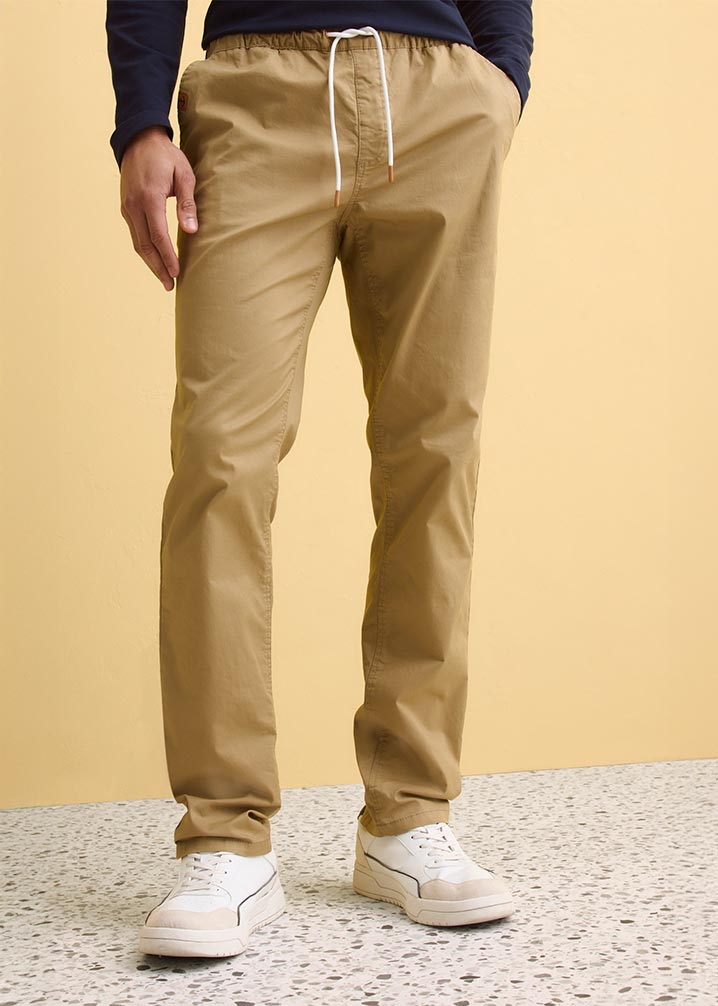 Beige Hose mit Kordelzug, dunkler Pullover und weiße Sneaker .