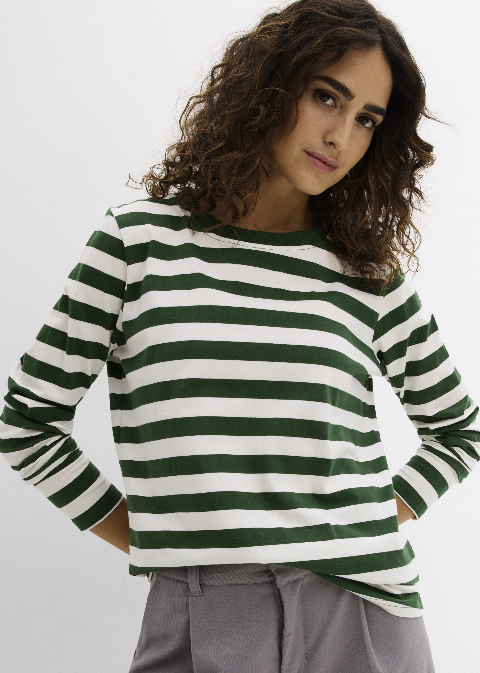 Ein grün-weiß gestreiftes Langarmshirt wird mit einer lässigen grauen Stoffhose kombiniert.