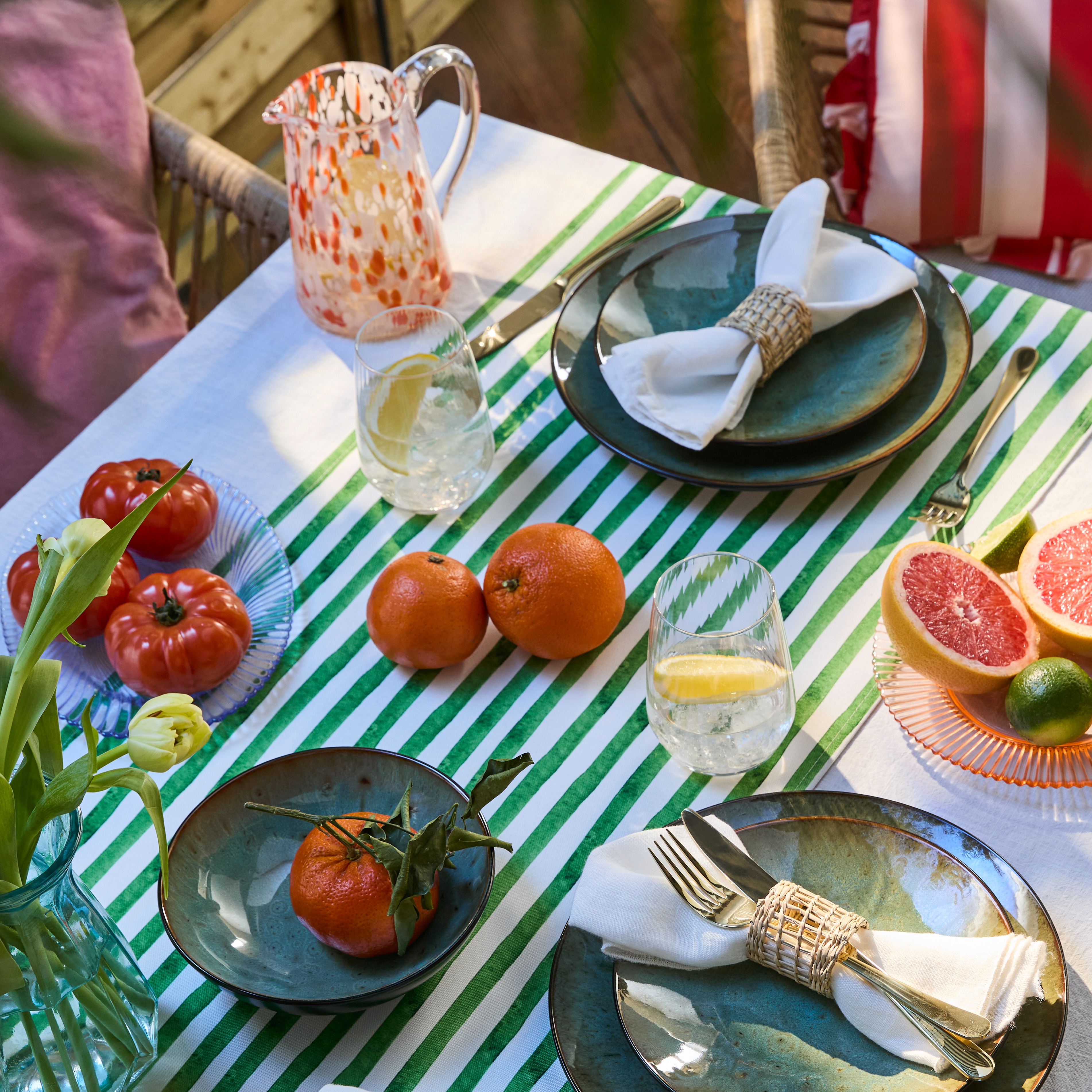 Ein gestreiftes Tischtuch schmückt den sommerlichen Tisch mit buntem Geschirr und frischem Obst.