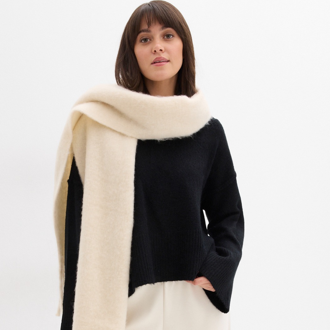 Schwarzer Pullover kombiniert mit cremefarbenem Schal.