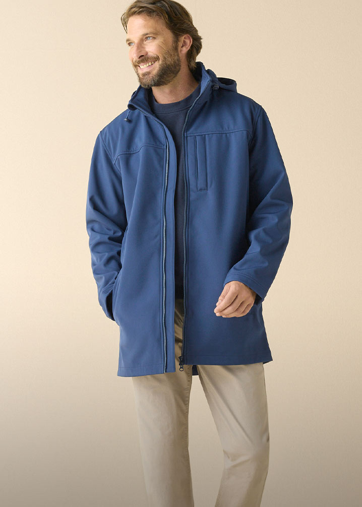 Mann trägt einen Softshell Parka über dunklem Shirt und beiger Hose.