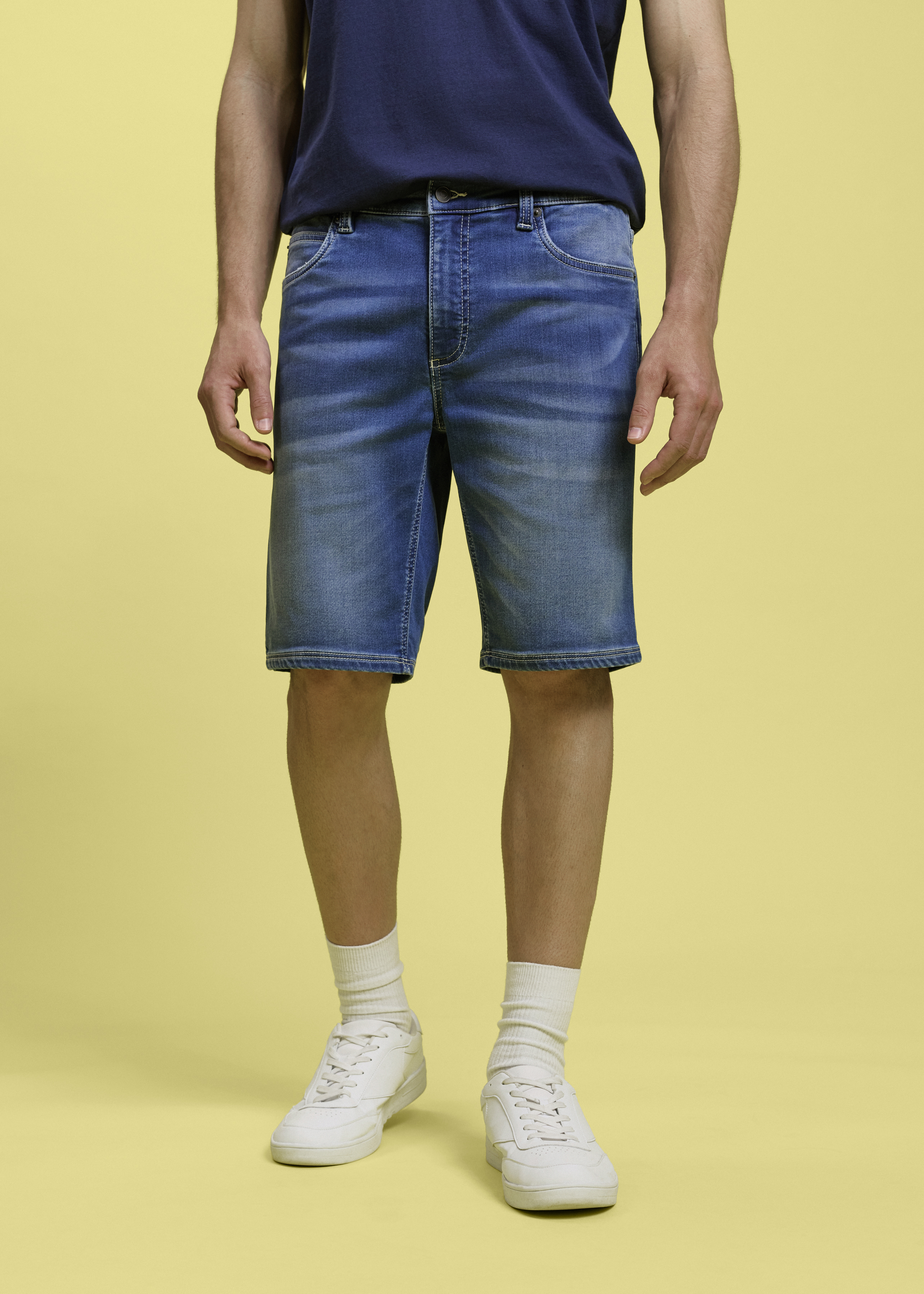 Lässige Jeans-Shorts und blaues T-Shirt kombiniert mit weißen Sneakers und Socken.