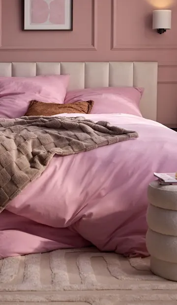 Rosa Bettwäsche, flauschige Decke und bunte Vorhänge schmücken dieses gemütliche Schlafzimmer.