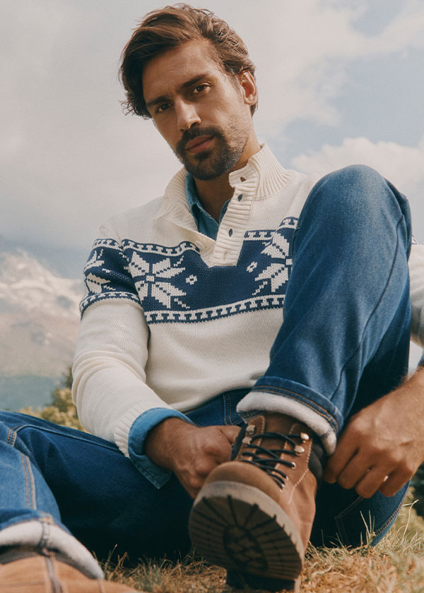 Ein gemütlicher Fair-Isle-Pullover, Jeans und robuste braune Wanderstiefel im Freien.