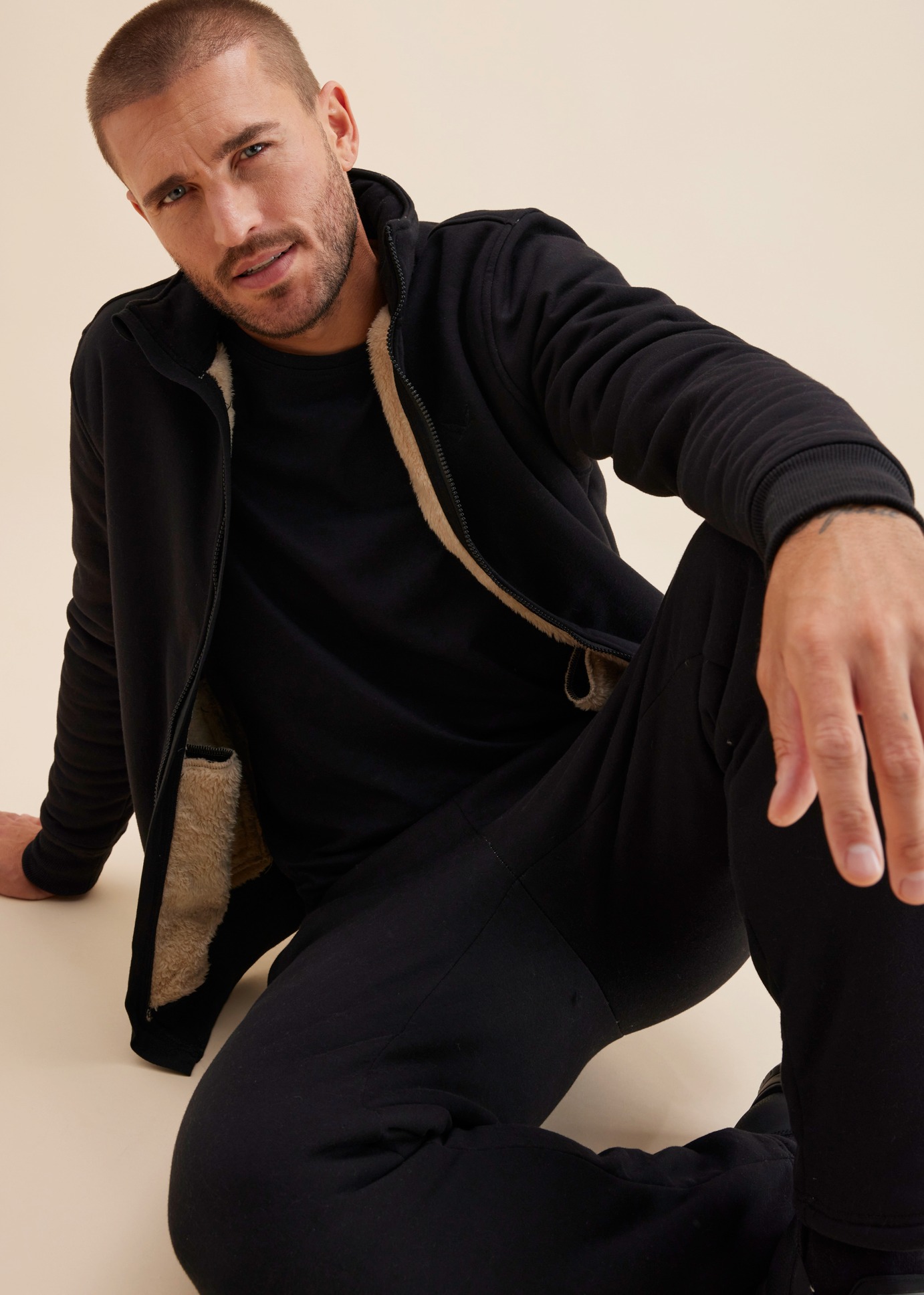 Er trägt schwarze Jogginghose, T-Shirt und eine warme Jacke mit Teddyfutter.