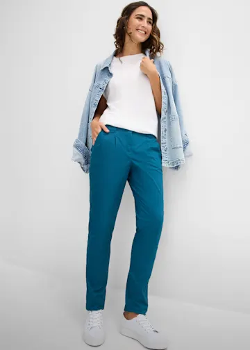 Türkisfarbene Hose, weißes Shirt, lässige Jeansjacke und weiße Sneaker.
