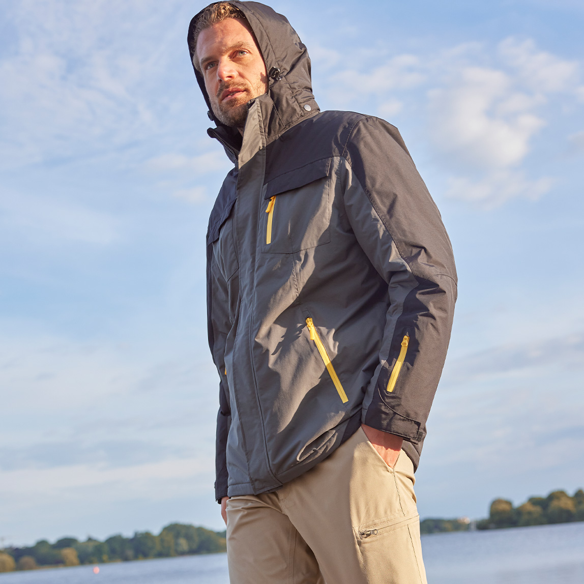 Graue Outdoorjacke mit gelben Reißverschlüssen und Kapuze.
