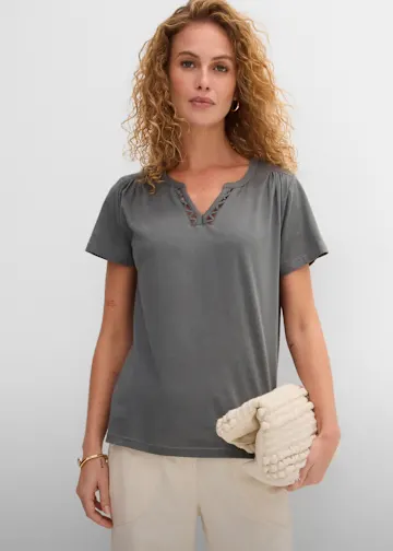 Graues T-Shirt mit V-Ausschnitt, helle Hose und strukturierte beige Clutch.