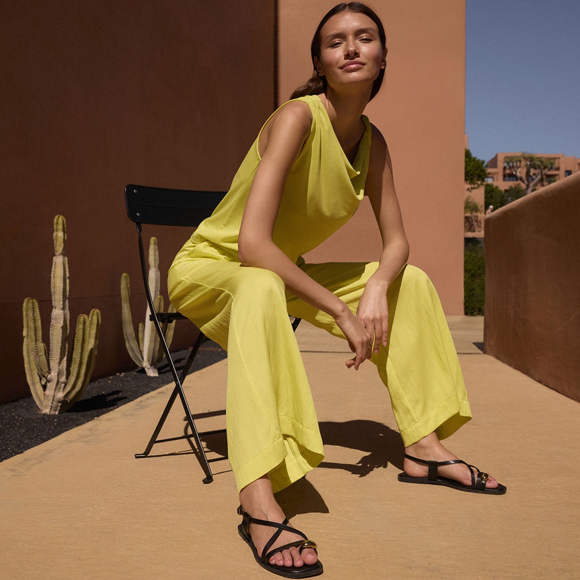Leuchtend gelbes Sommeroutfit: Ärmelloses Top und weite Hose. Schwarze Sandalen vervollständigen den Look.