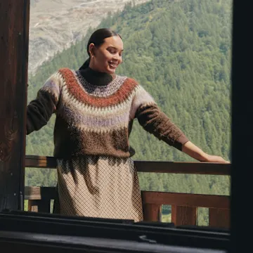 Sie trägt einen warmen, bunten Strickpullover mit Muster und einen passenden Rock.