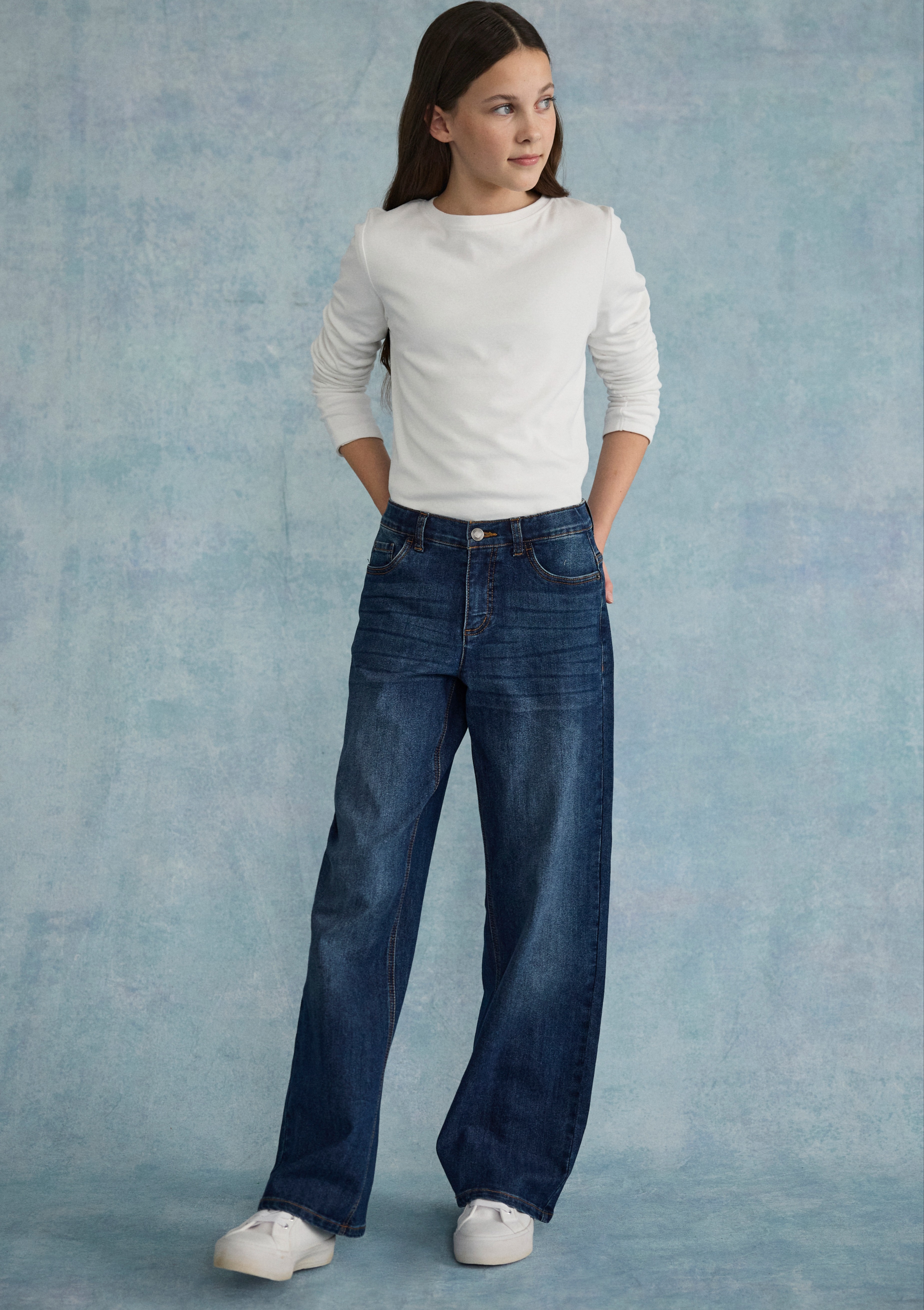 Weißer Pullover kombiniert mit weiten Jeans und sportlichen weißen Sneakers.