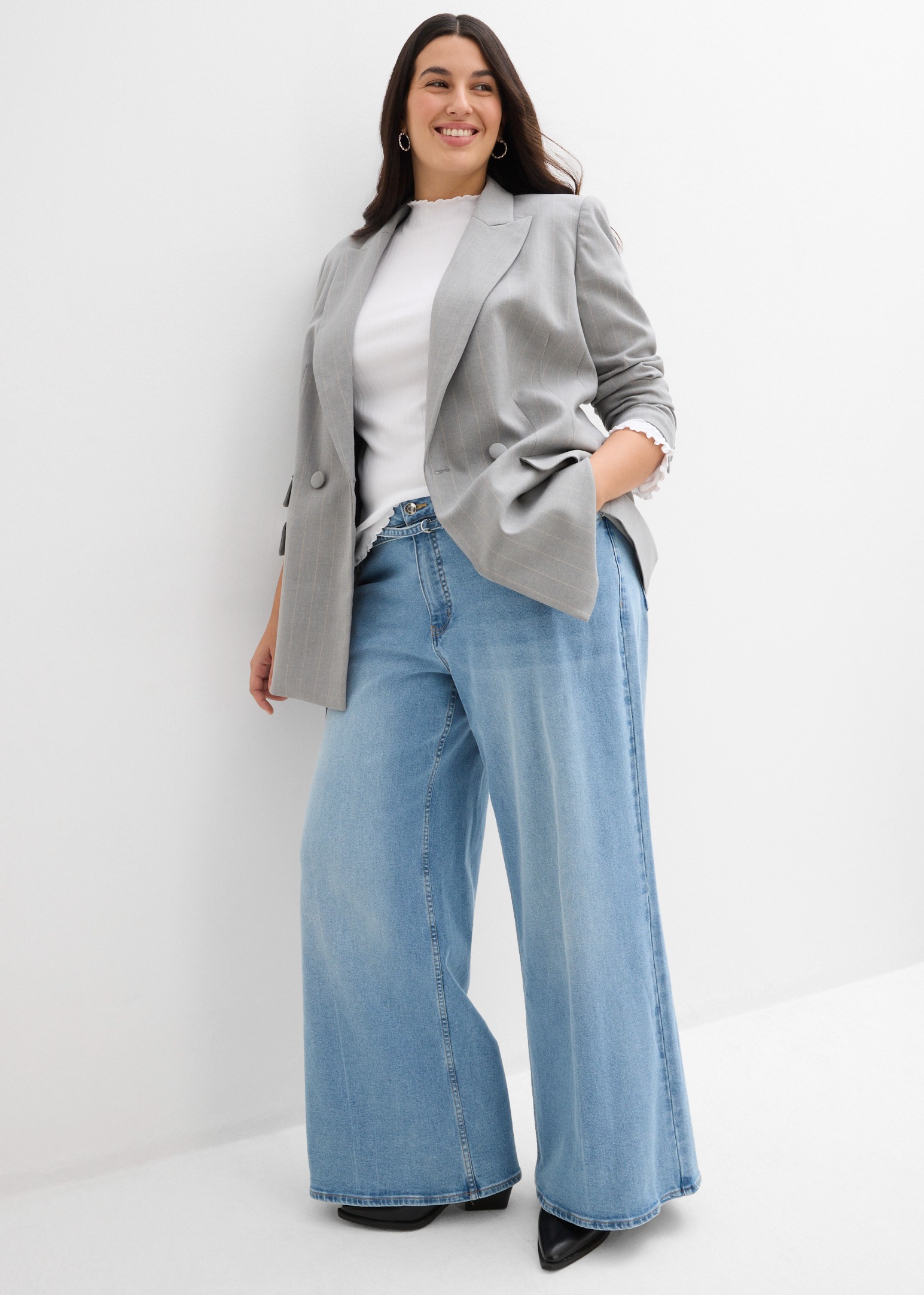 Eleganter grauer Blazer, weißes Oberteil und weite Jeans.