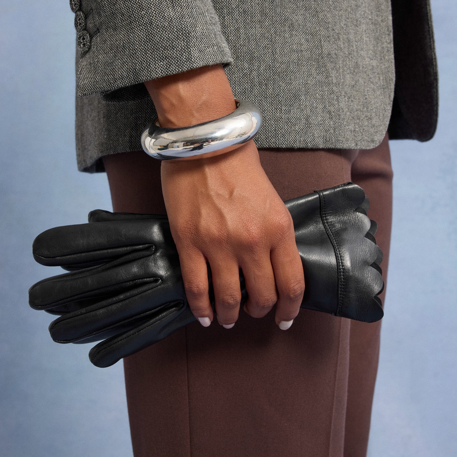 Eleganter grauer Mantel, braune Hose und schwarze Lederhandschuhe. 