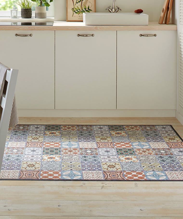 Ein bunter Teppich mit geometrischen Mustern schmückt den Boden vor weißen Küchenschränken.
