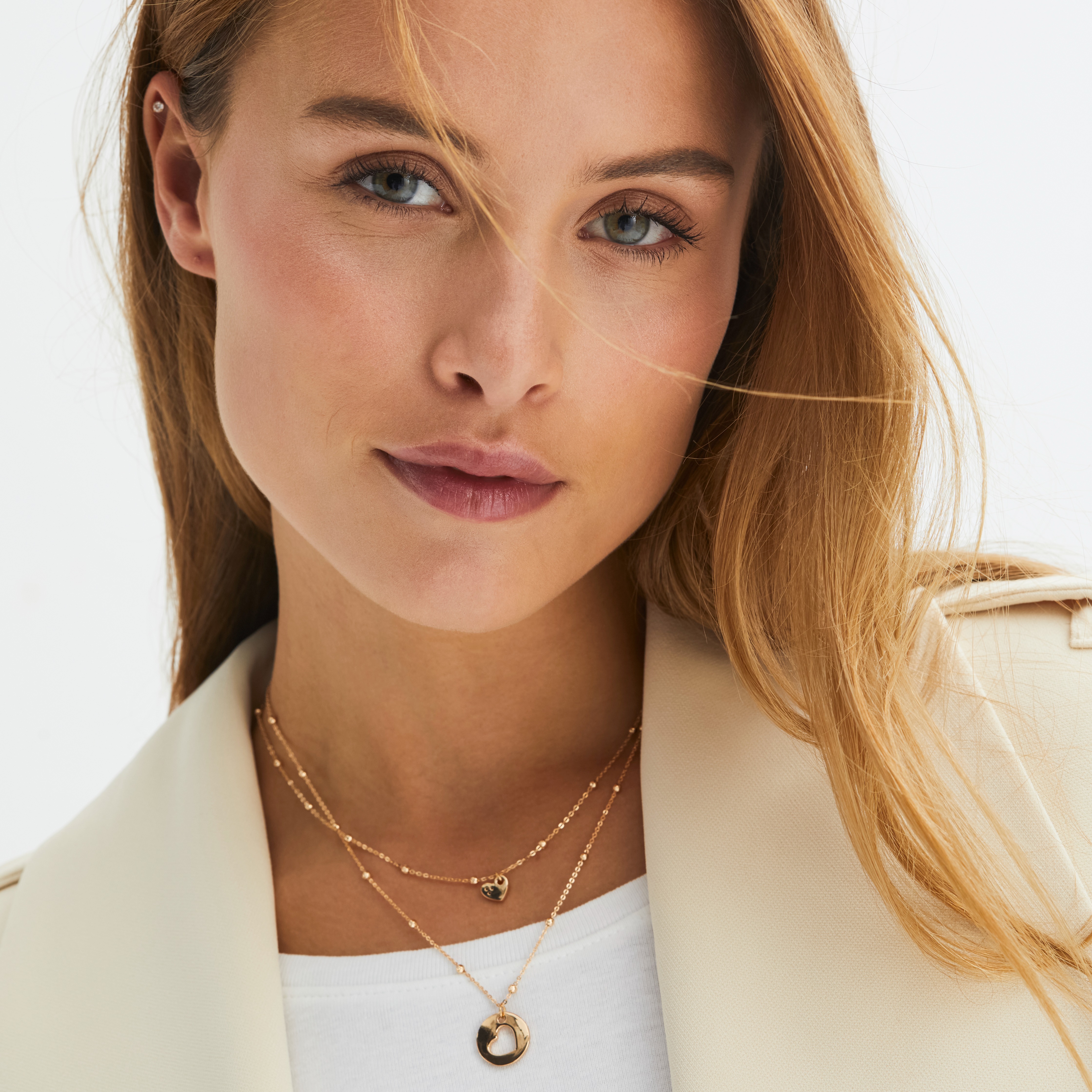 Die Frau trägt einen hellen, beigen Blazer mit einer Kette.