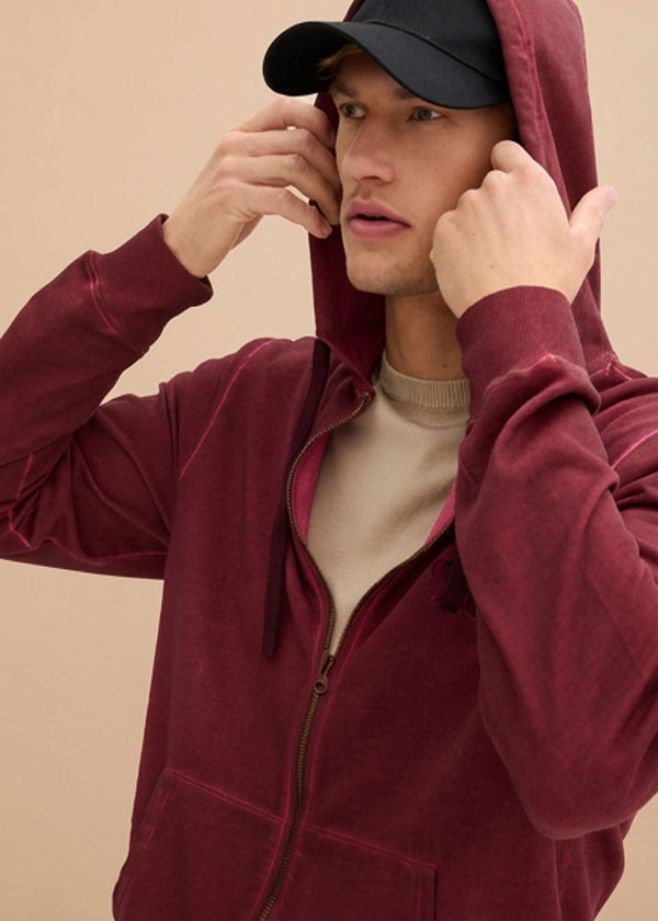 Lässiger Look mit weinrotem Hoodie, beigem Shirt und schwarzer Kappe.