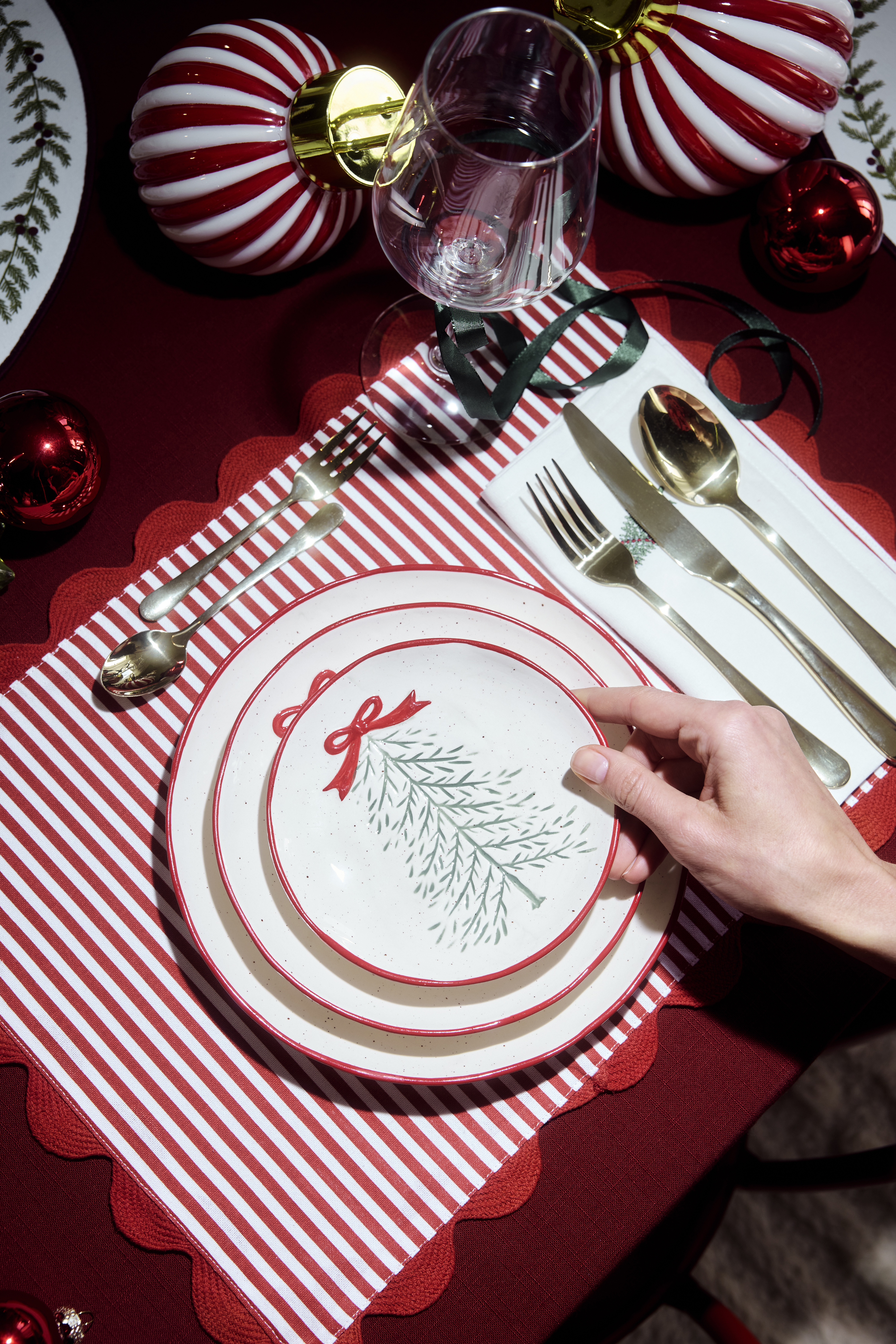 Weihnachtlich gedeckter Tisch: rote Tischdecke, gestreiftes Set, Teller, Besteck und Kugeln.