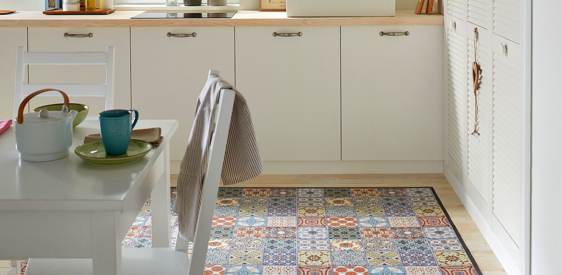 Moderne Küche mit buntem Fliesenboden. Weiße Schränke und Arbeitsplatte. Handtuch hängt an Schublade.