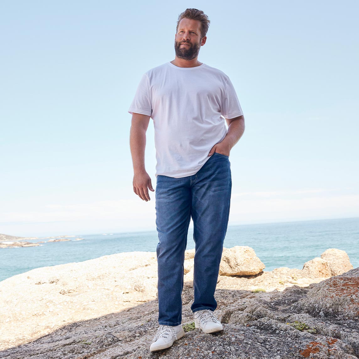 Weißes T-Shirt, blaue Jeans und weiße Sneakers am Strand.