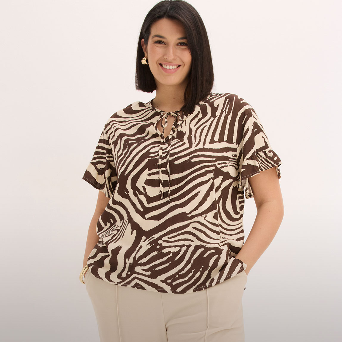 Modische Bluse mit Zebramuster und Bindedetail, dazu hellbeigefarbene Hose.