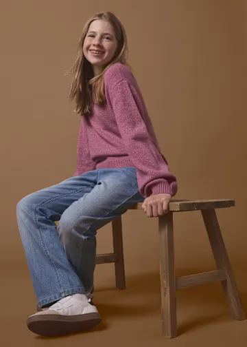 Rosa Pullover, blaue Jeans und helle Sneaker.