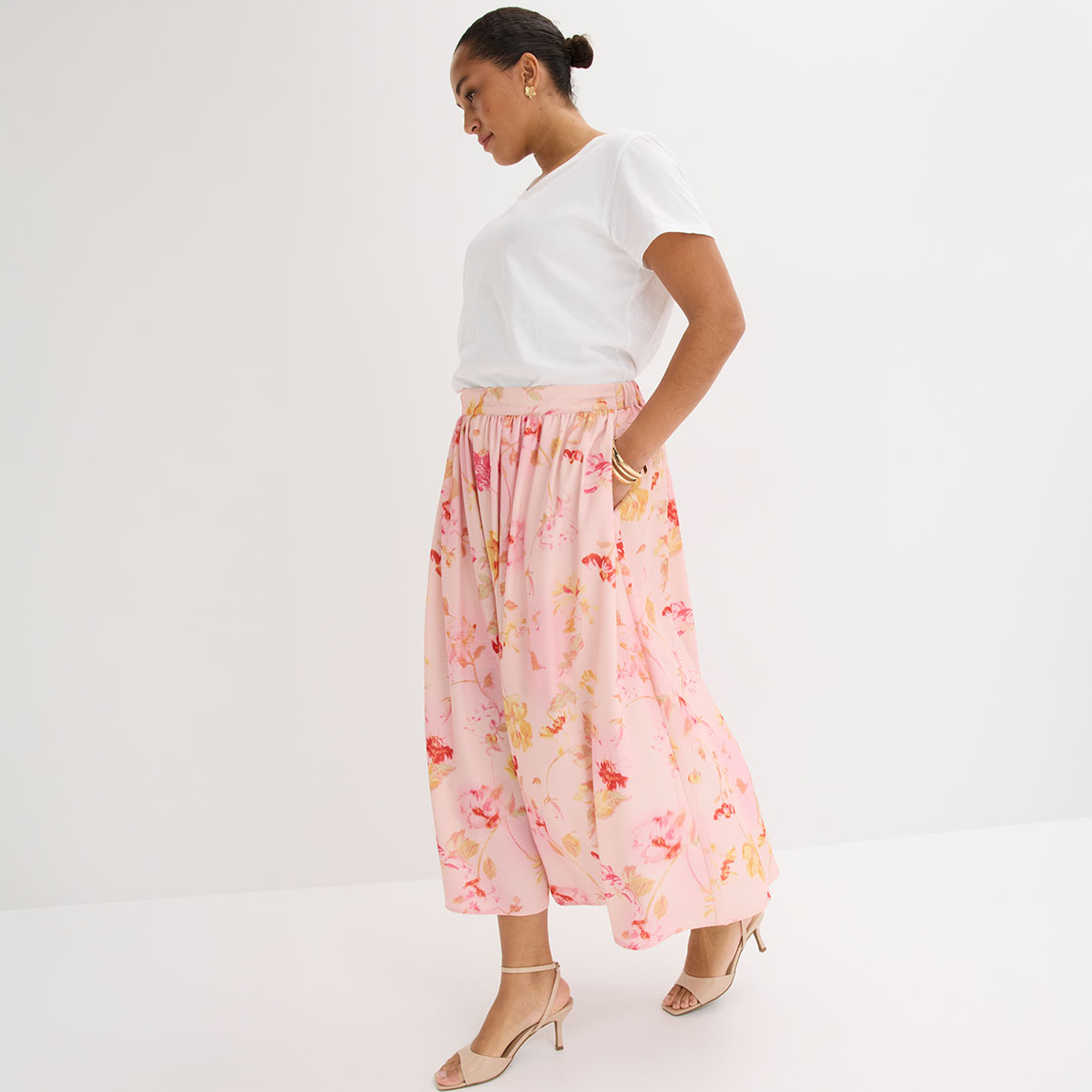 Weißes T-Shirt kombiniert mit rosa geblümtem Maxirock und beigen Sandalen.