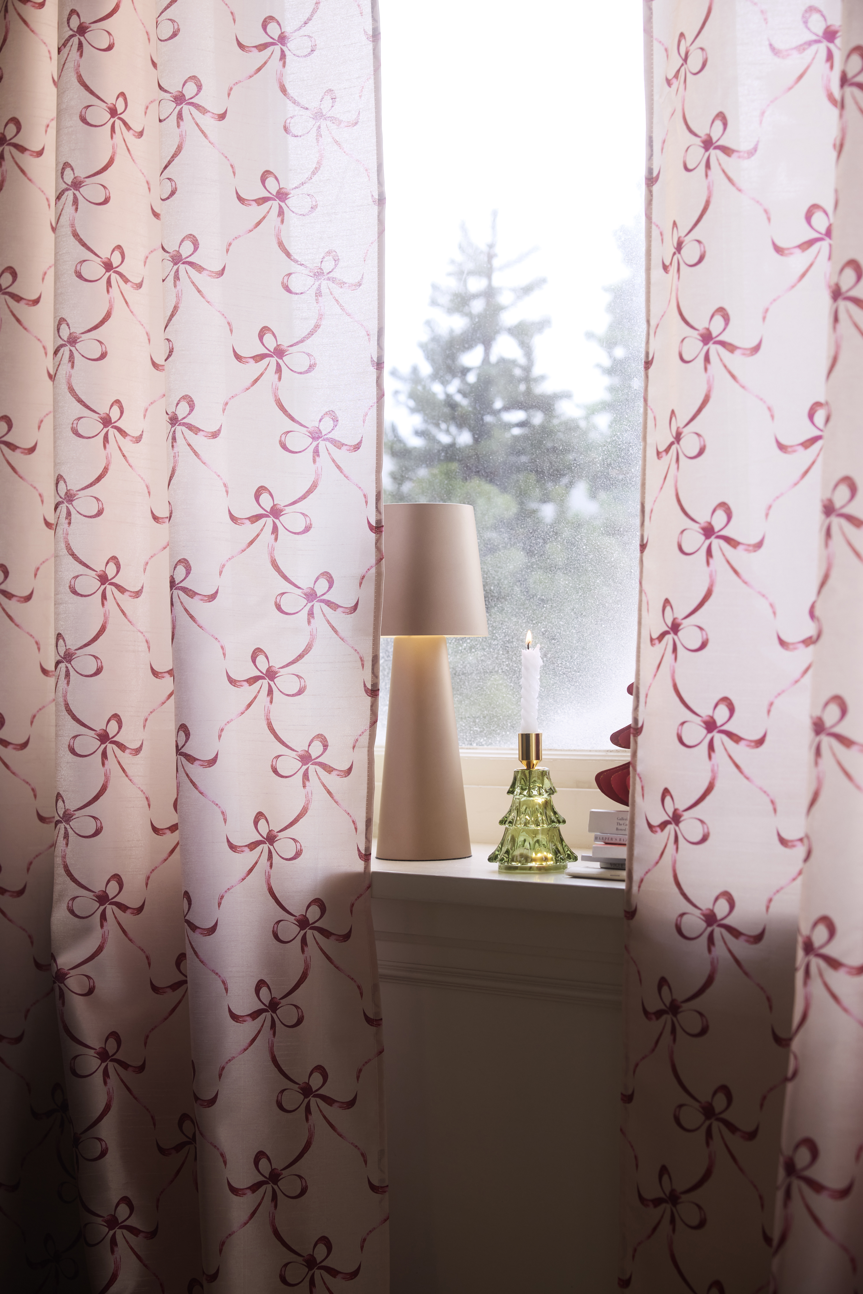 Rosa Vorhänge mit Schleifenmuster schmücken das Fenster zusammen mit Lampe und Kerze.