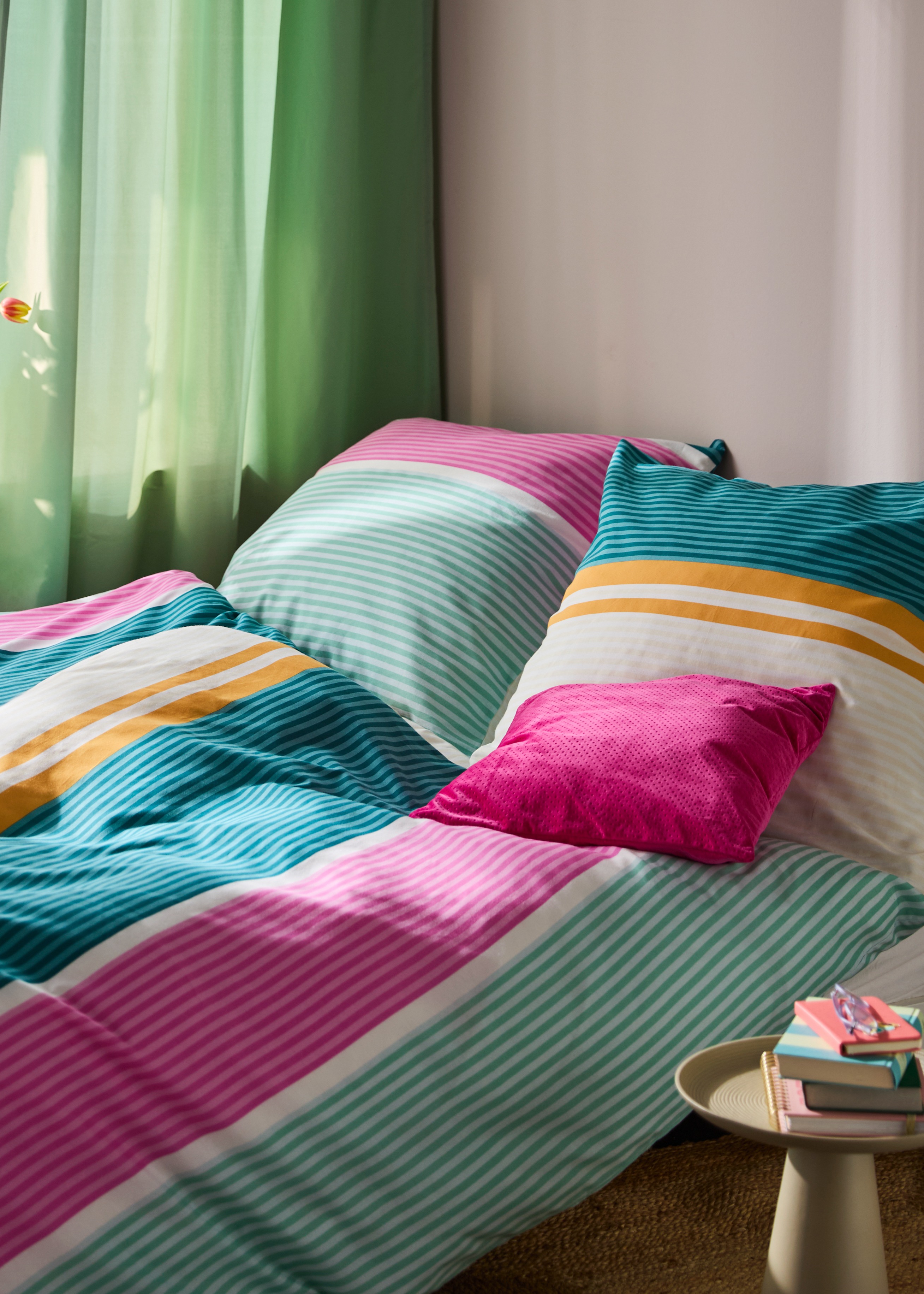 Bunte Bettwäsche mit Streifen in Pink, Grün und Orange schmückt das gemütliche Bett.