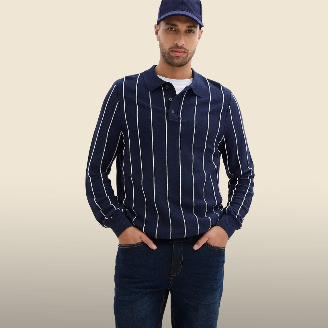 Blaue Kappe, gestreiftes Langarm-Poloshirt und dunkle Jeans bilden einen lässigen Look.