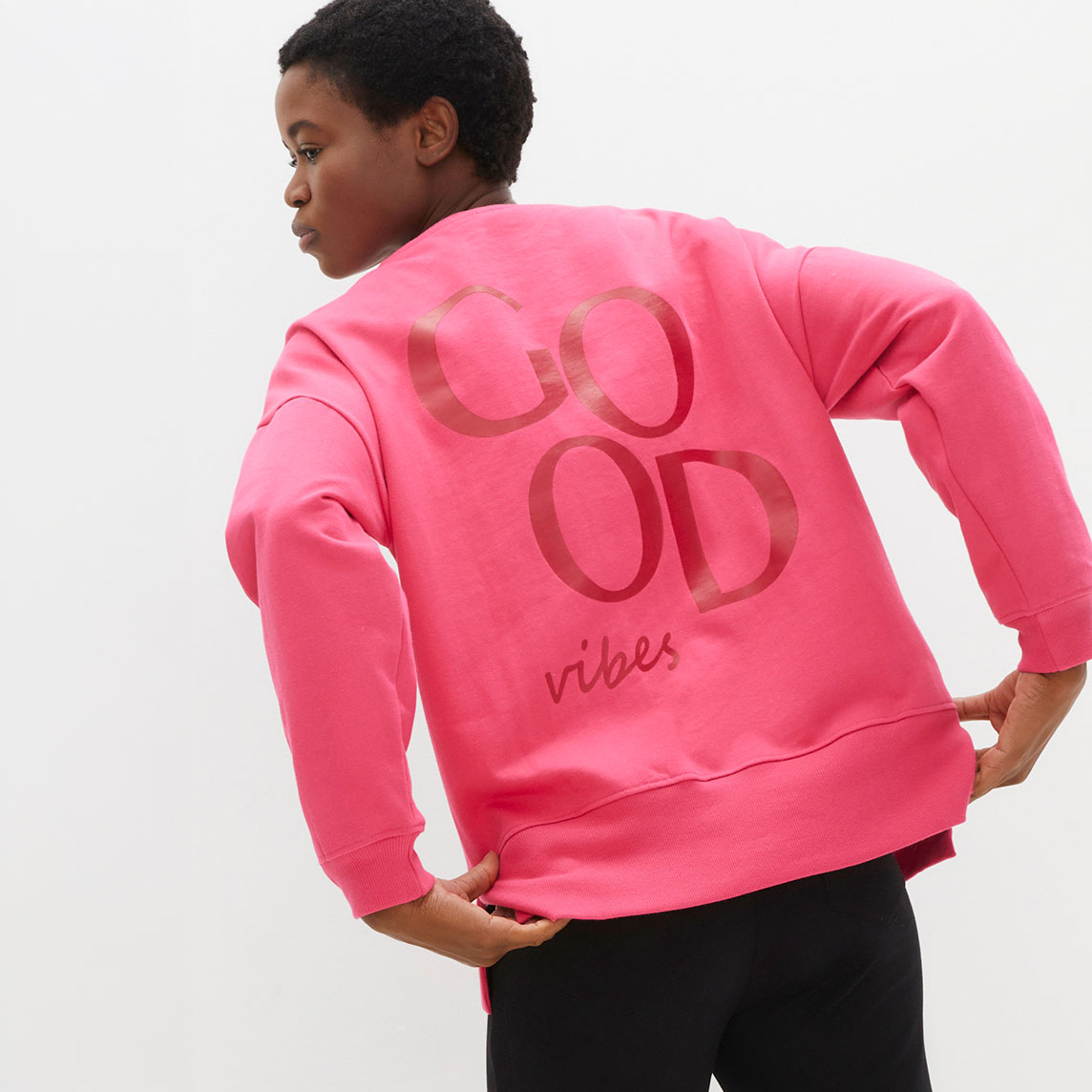 Rosa Sweatshirt mit "Good Vibes" Aufdruck kombiniert mit schwarzer Hose für einen lässigen Look.