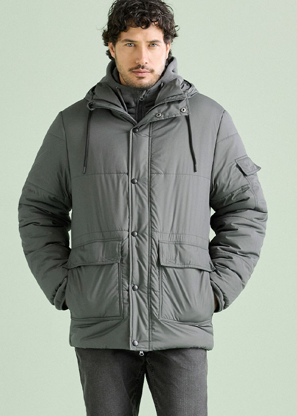 Mann trägt eine graue, wattierte Winterjacke mit Kapuze und dunkler Hose.