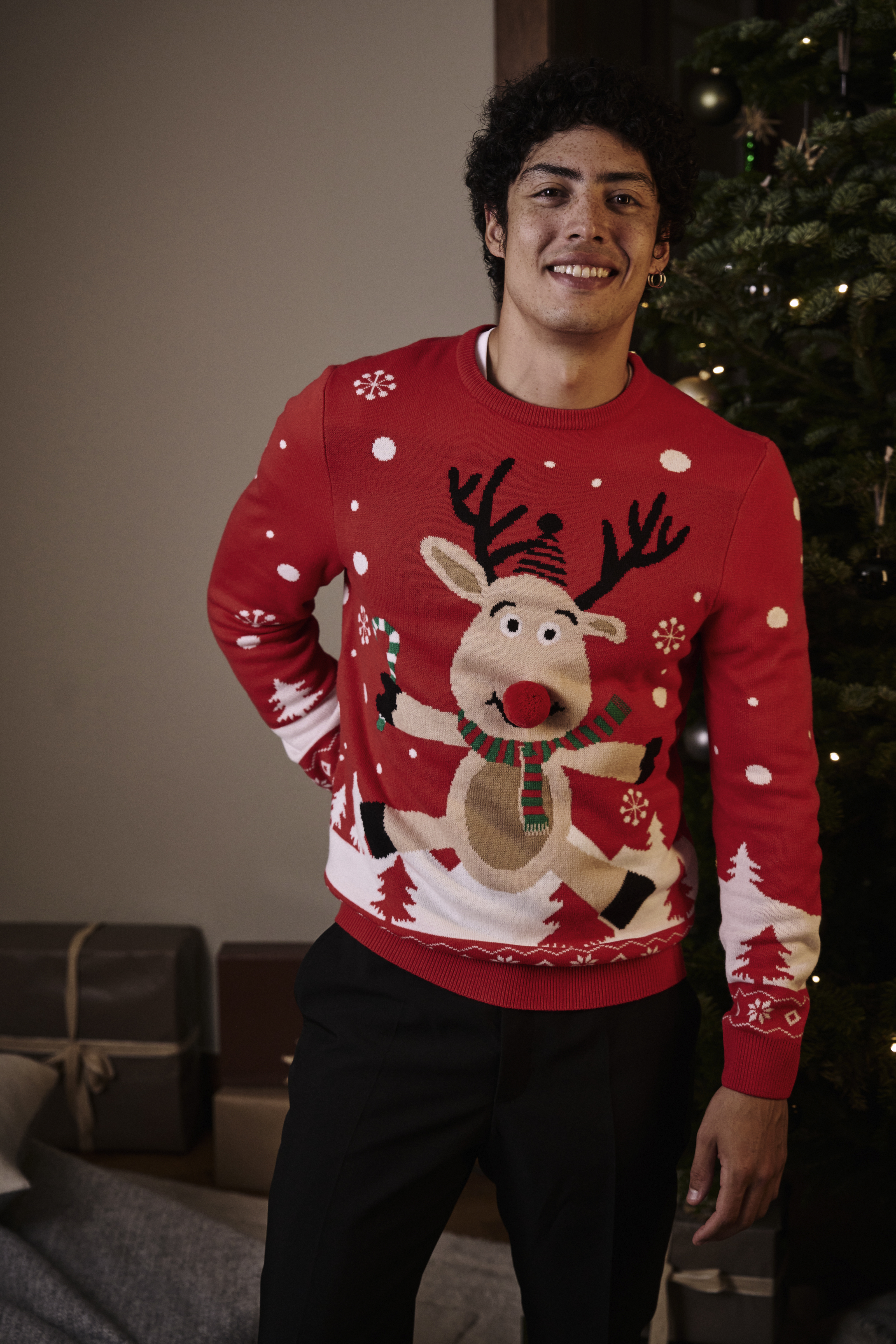 Ein roter Weihnachtspullover mit lustigem Rentiermotiv und schwarze Hose.