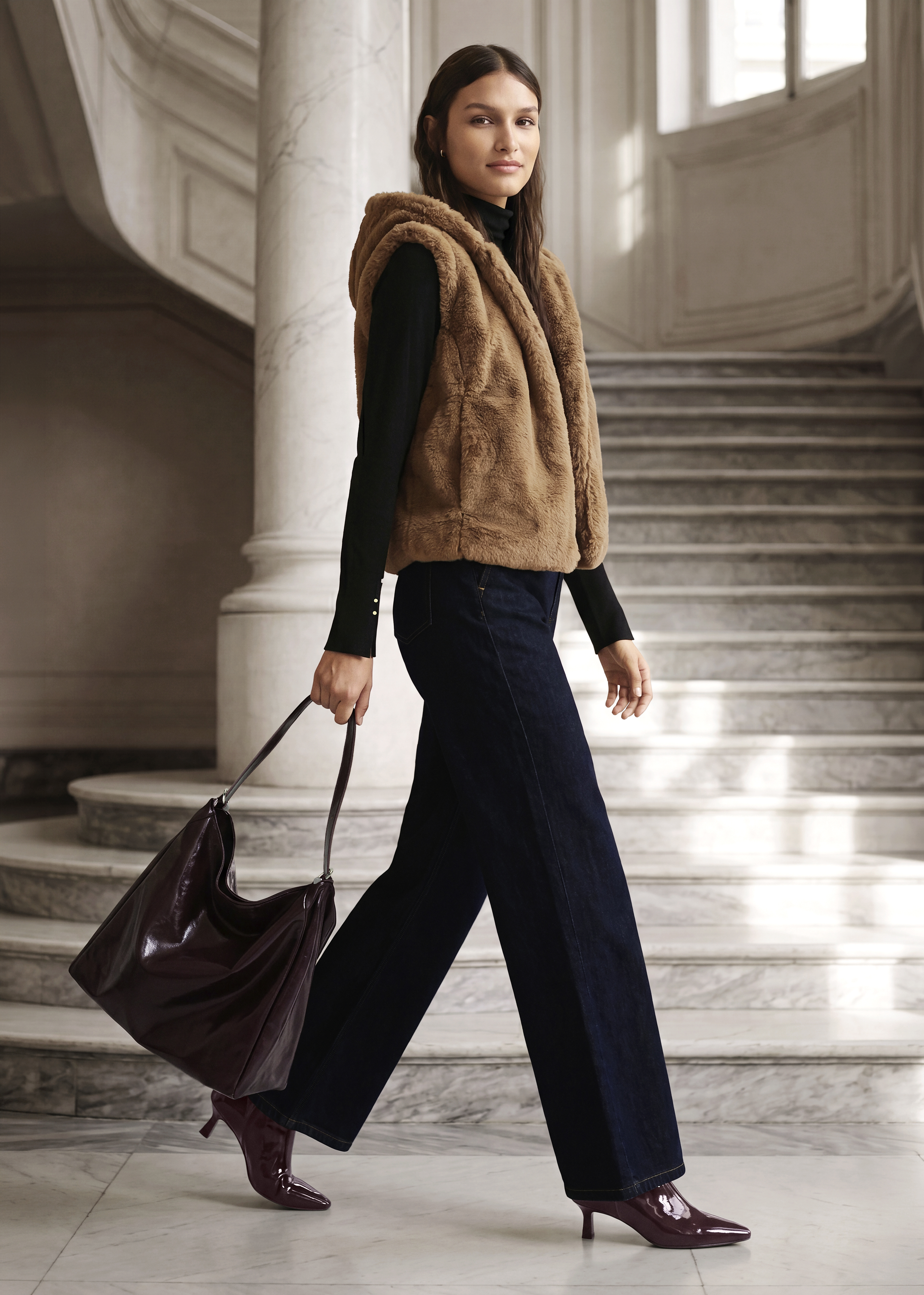 Braune Fellweste, schwarzer Rolli, weite Jeans, burgunderfarbene Tasche und Stiefeletten.