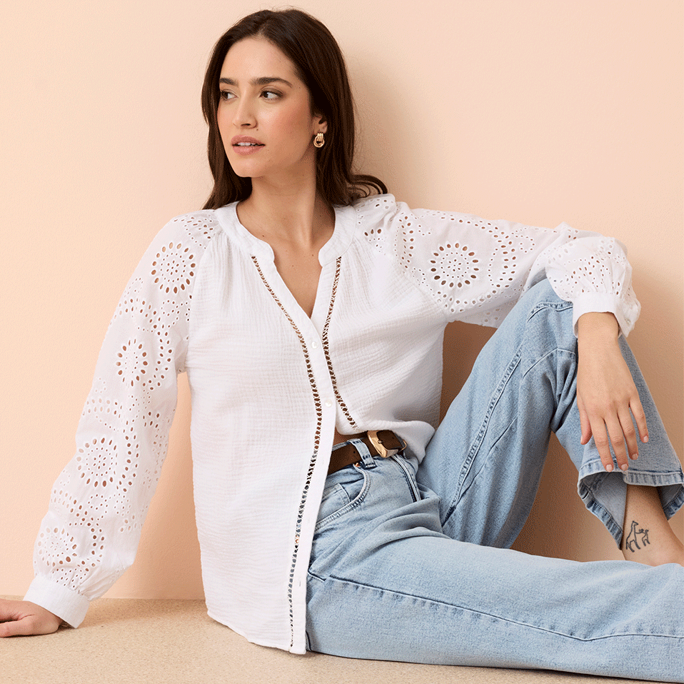 Weiße Lochstickerei-Bluse mit langen Ärmeln, kombiniert mit hellblauen Jeans und einem Gürtel.